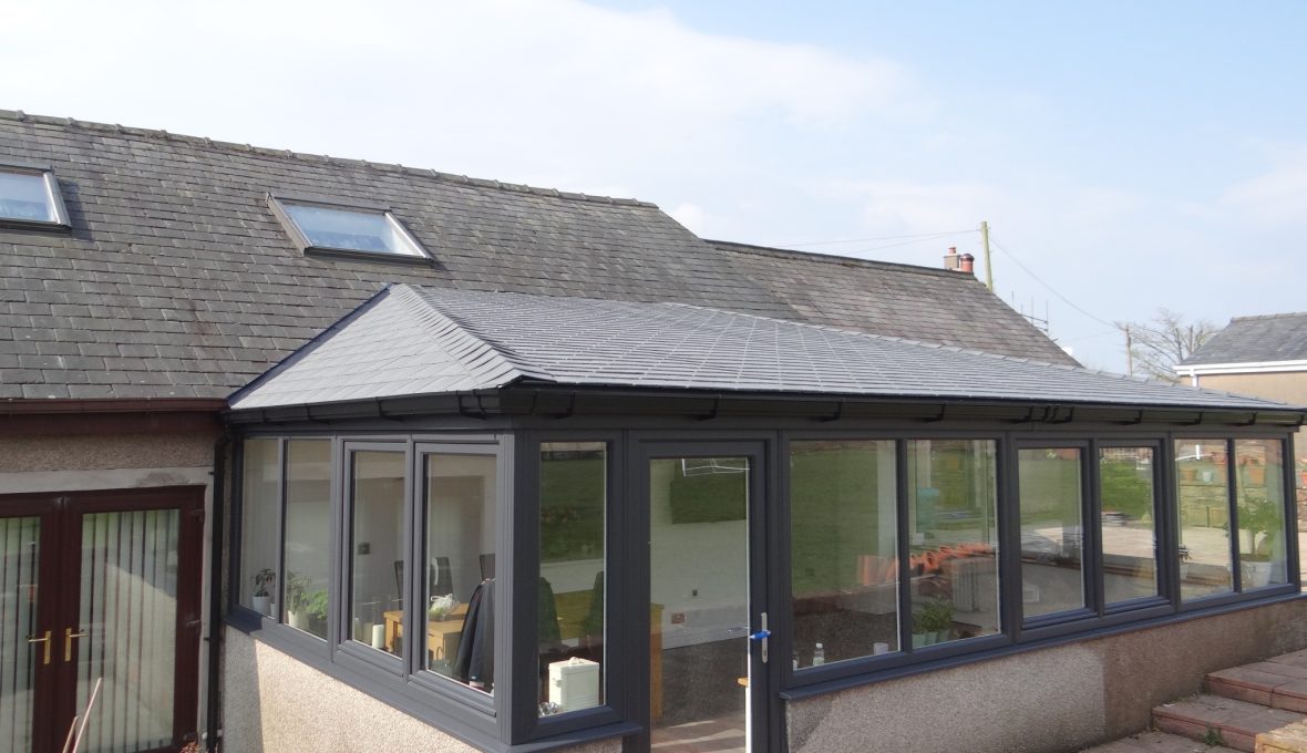 Grey slate warm/solid roof conservatory extension on a sunny day with a blue sky.