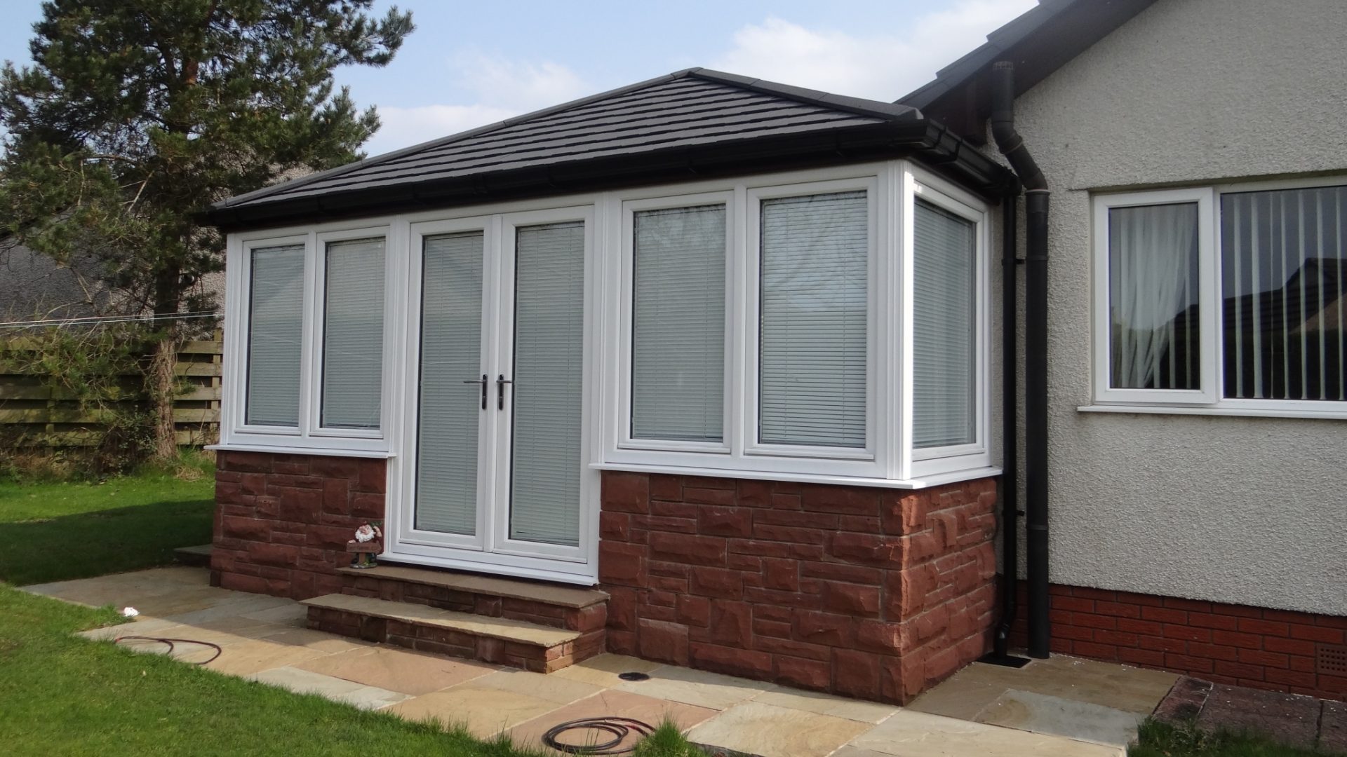 A solid roof conservatory extension, with a black slate tiled roof, on a sunny day.