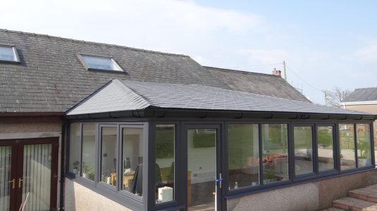 Grey slate warm/solid roof conservatory extension on a sunny day with a blue sky.