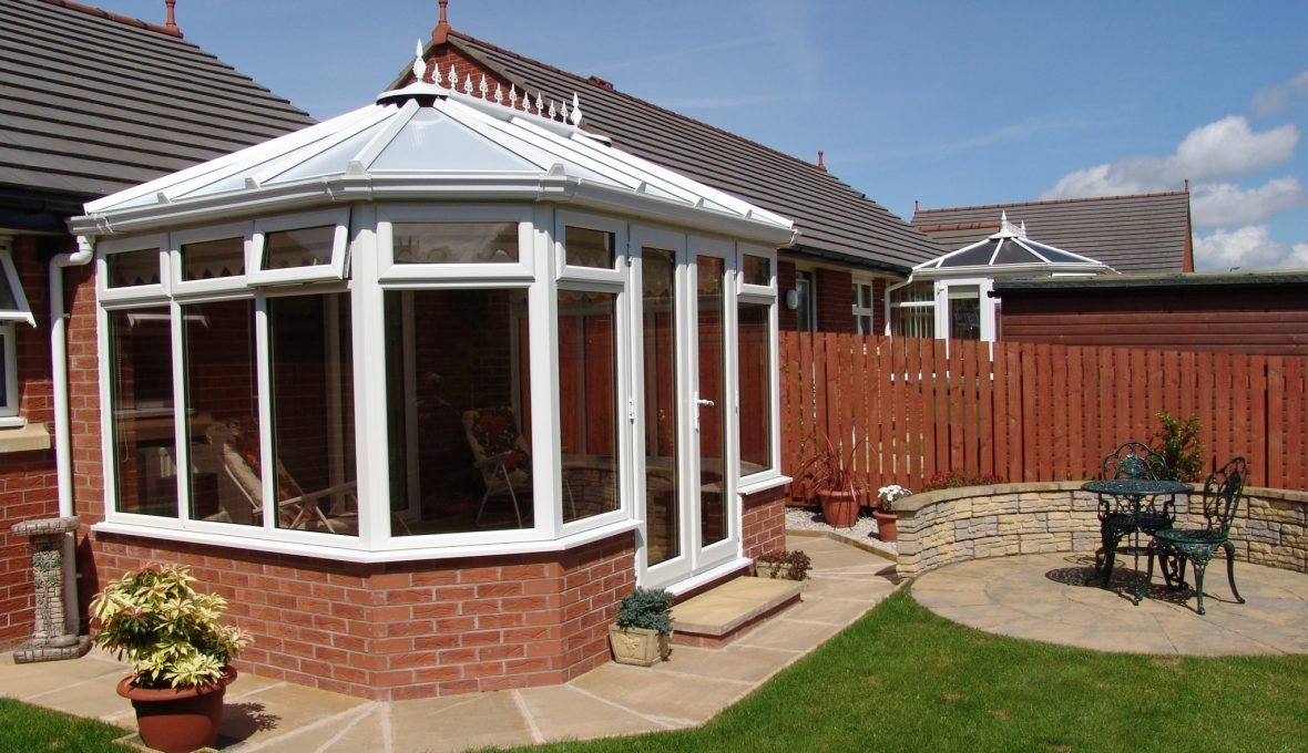 A traditional conservatory extension on a home with white frames and glass roof on a summers day with a blue sky, installed by Keswick Superglaze in West Cumbria.