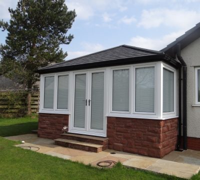 A solid roof conservatory extension, with a black slate tiled roof, on a sunny day.