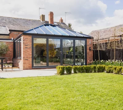 Back garden of home extension, featuring an Ultraframe hup! extension, with brick walls and black window frames.