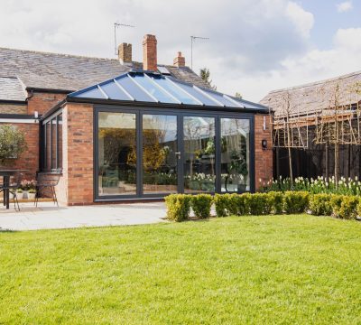 Back garden of home extension, featuring an Ultraframe hup! extension, with brick walls and black window frames.