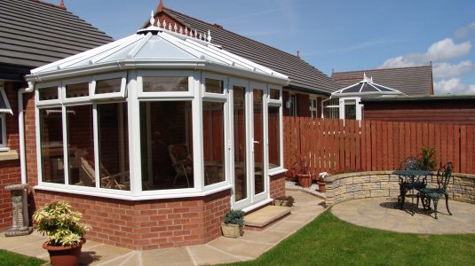 A traditional conservatory extension on a home with white frames and glass roof on a summers day with a blue sky, installed by Keswick Superglaze in West Cumbria.